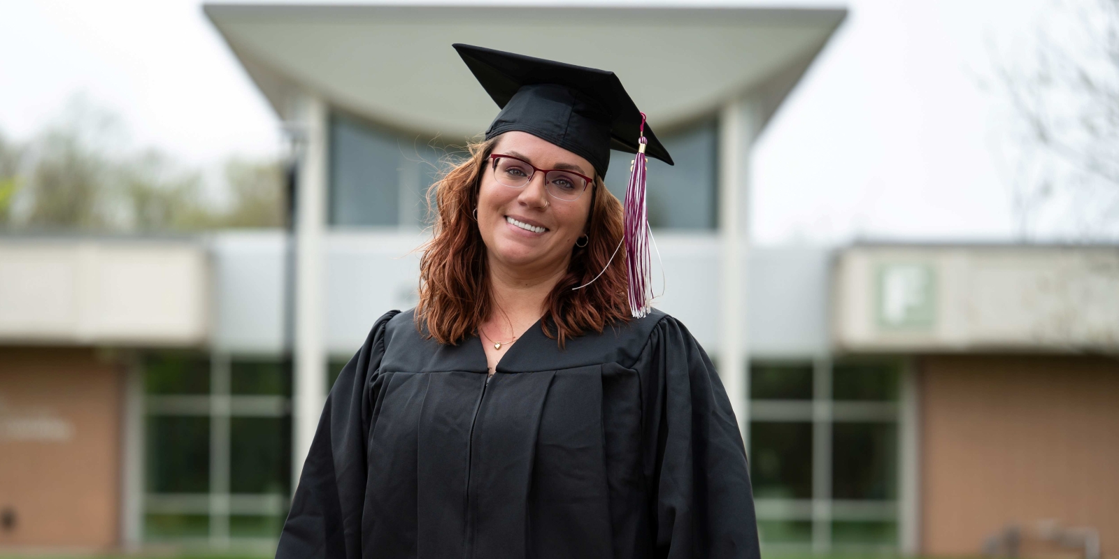 Adult student in grad attire in front of Founders Hall