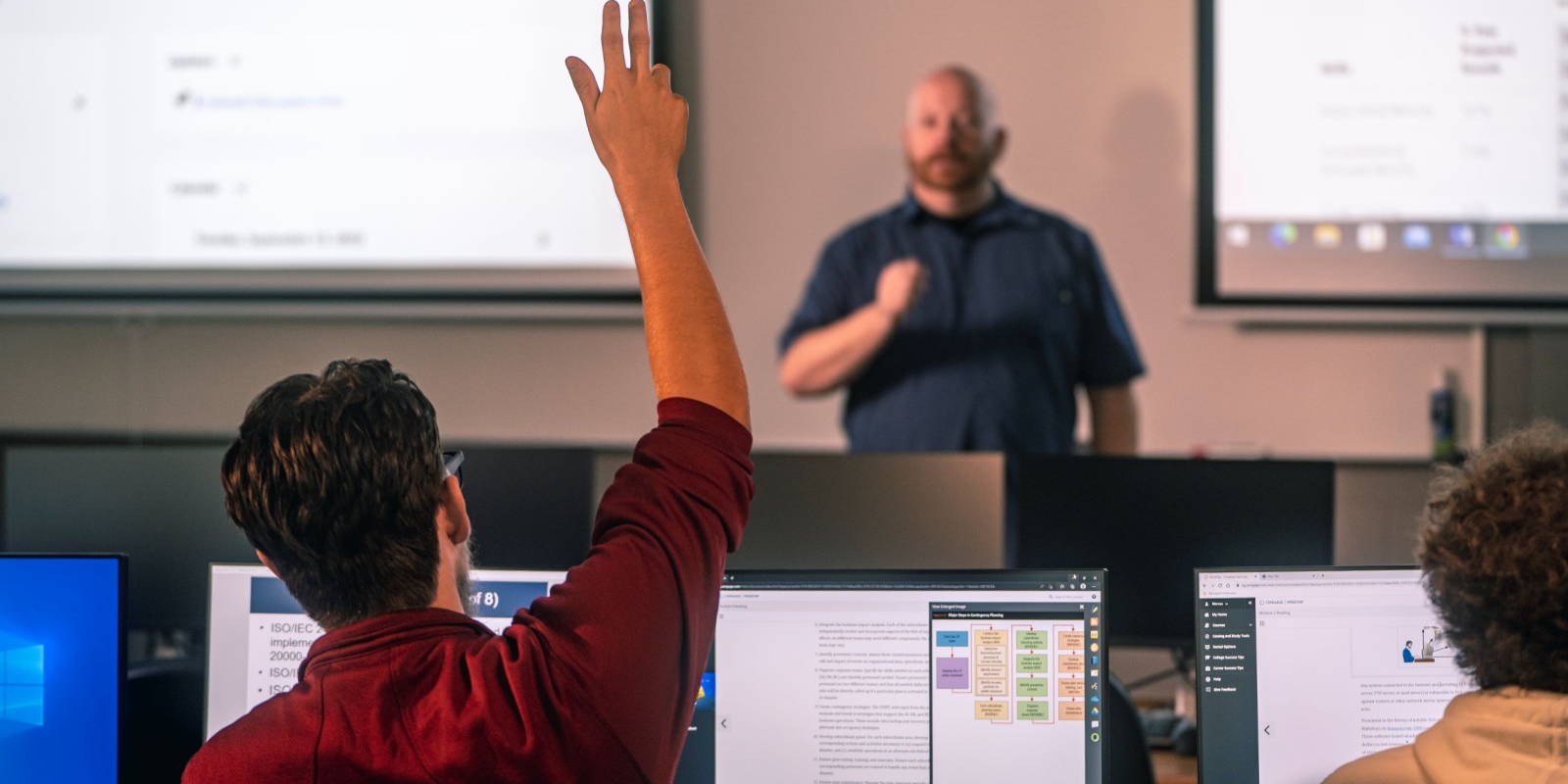 Student raising hand in class as instructed teaches